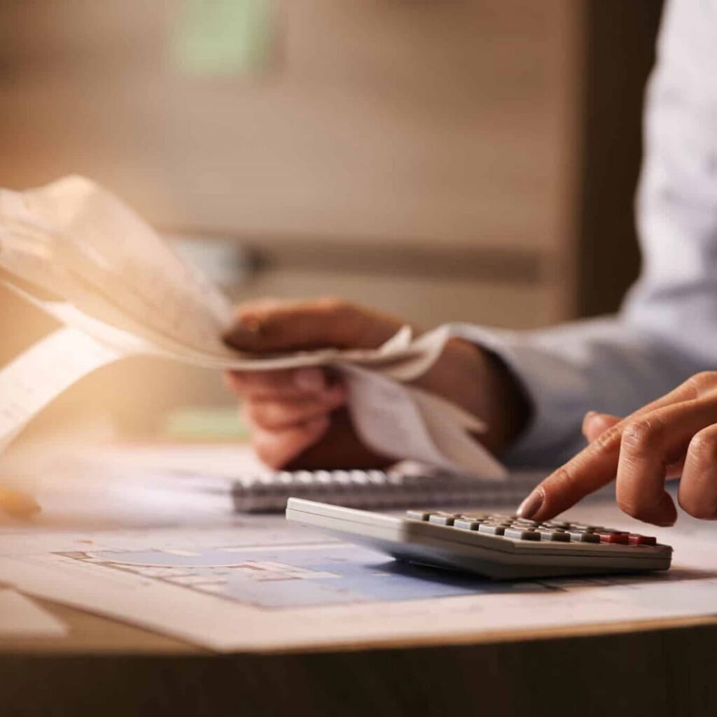 Pessoa usando uma calculadora e analisando documentos financeiros sobre uma mesa, com foco em planejamento contábil ou fiscal.