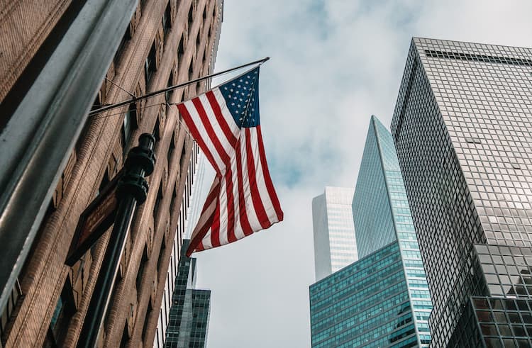 Bandera de Estados Unidos colgada en un edificio del distrito financiero, rodeada de rascacielos modernos en un día nublado