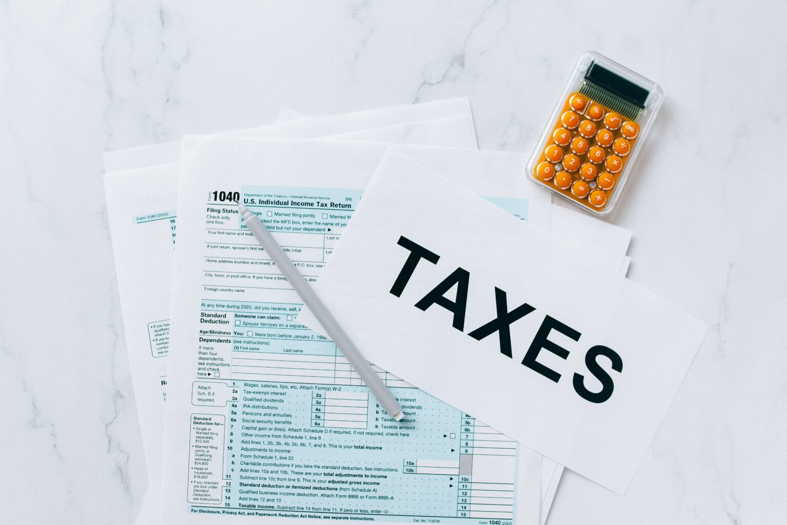 Mesa de mármore com formulários de imposto de renda nos EUA, caneta, calculadora e folha escrito "Taxes"