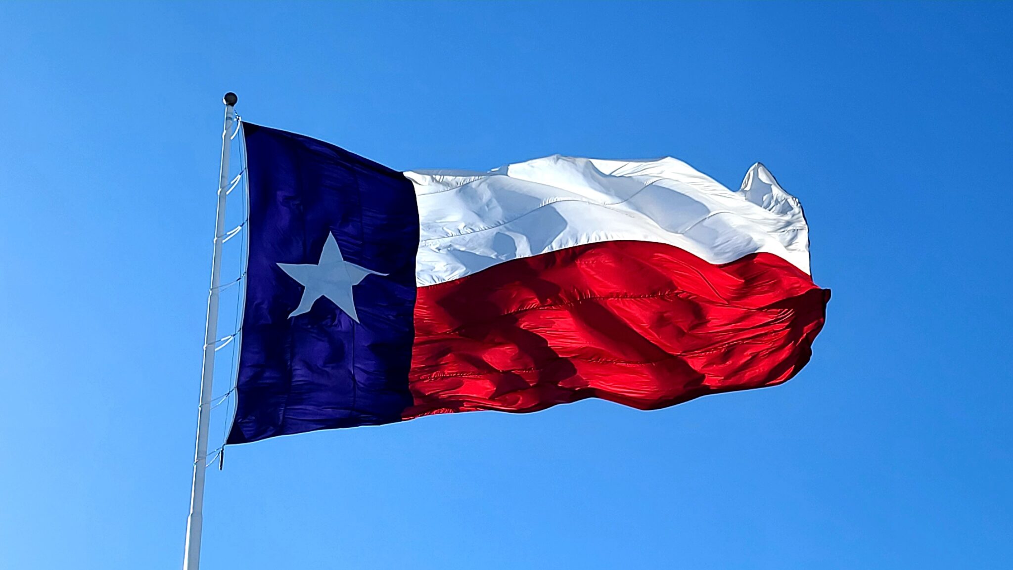 Texas flag under a bright blue sky.