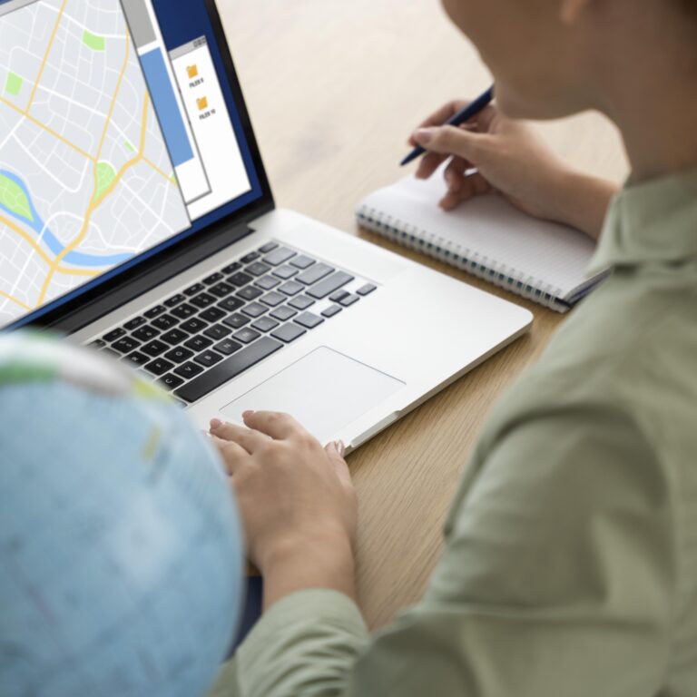 woman looking at computer with maps open and a globe next to it.