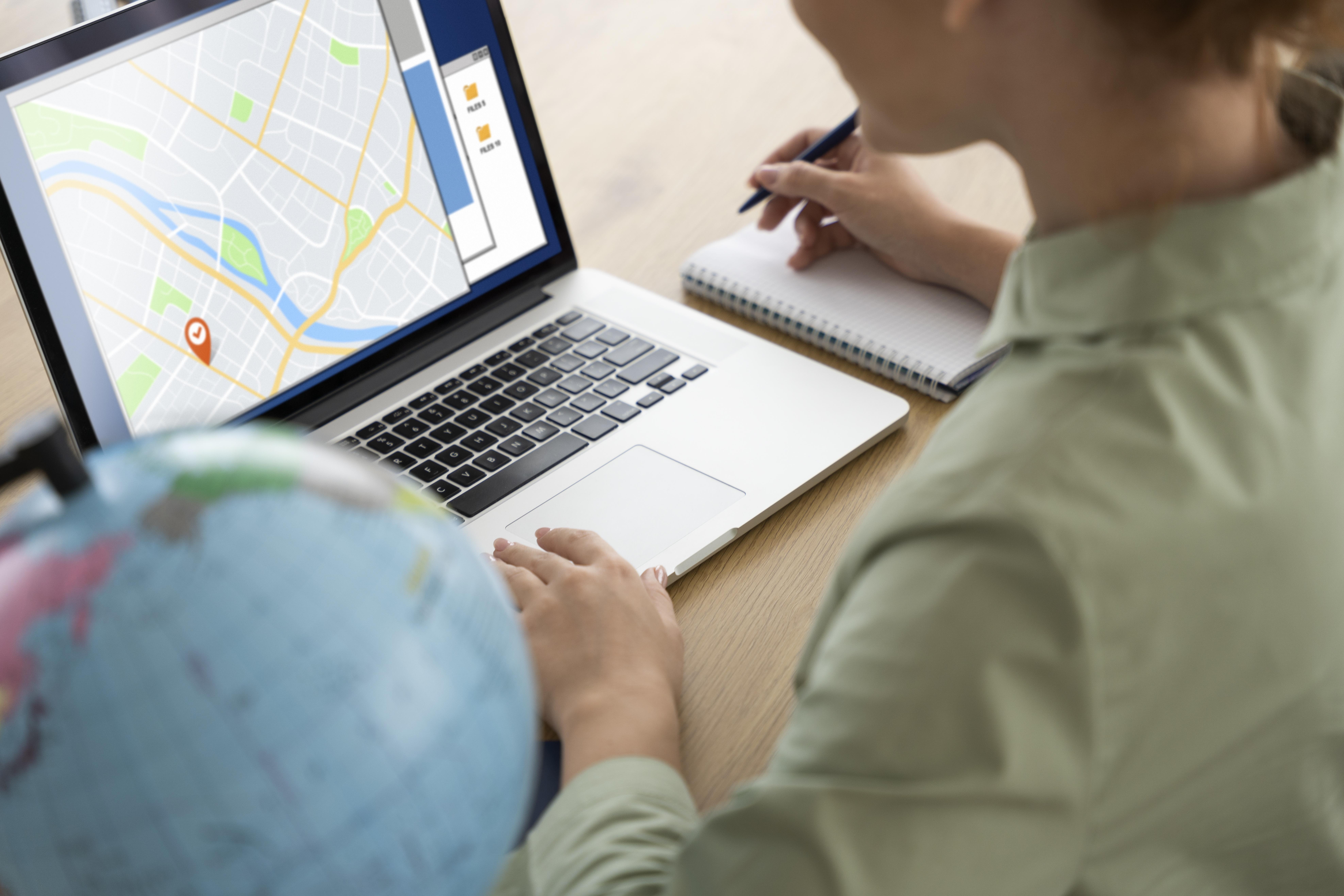 woman looking at computer with maps open and a globe next to it.