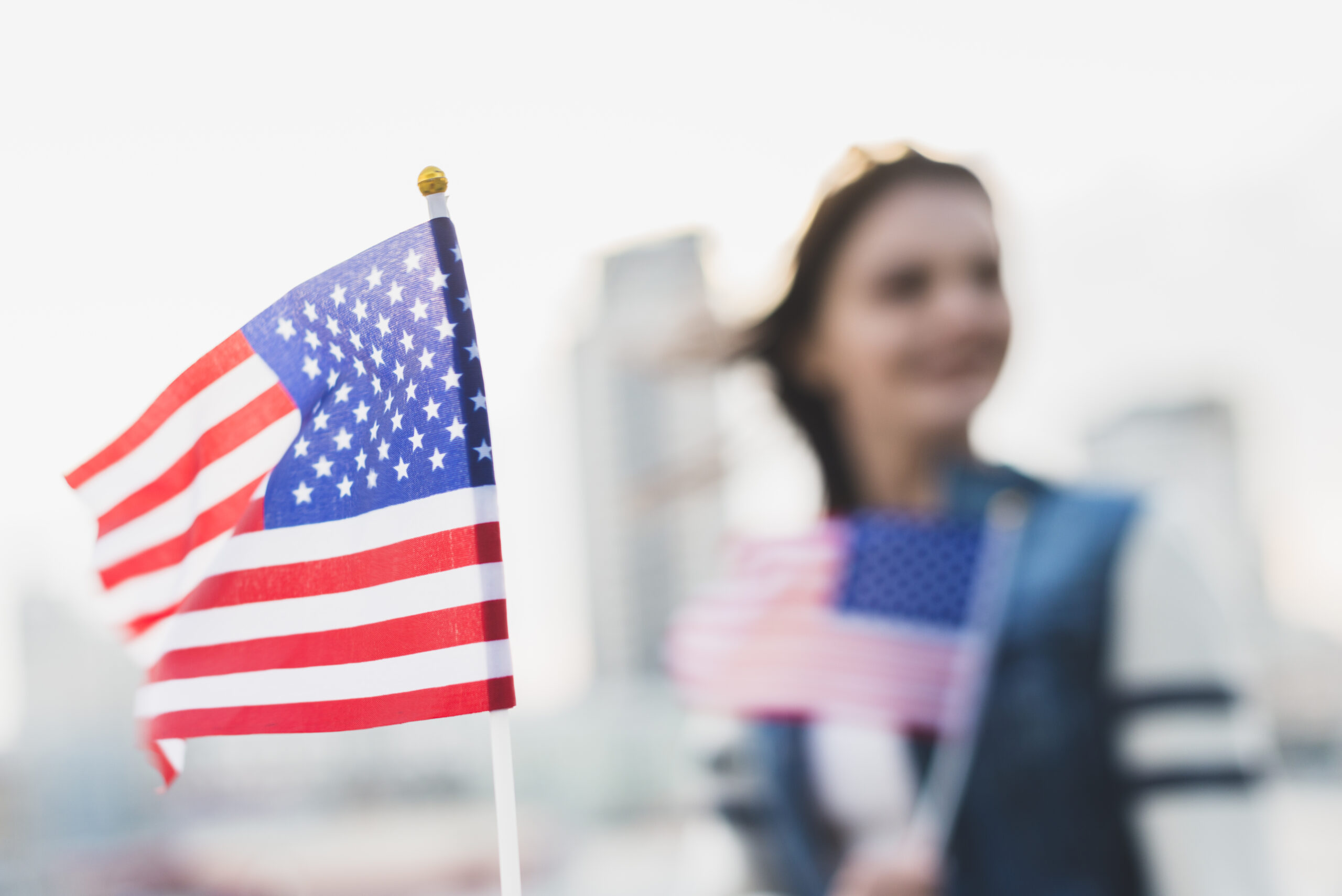 Woman holding a US flag in fron ot another US flag.