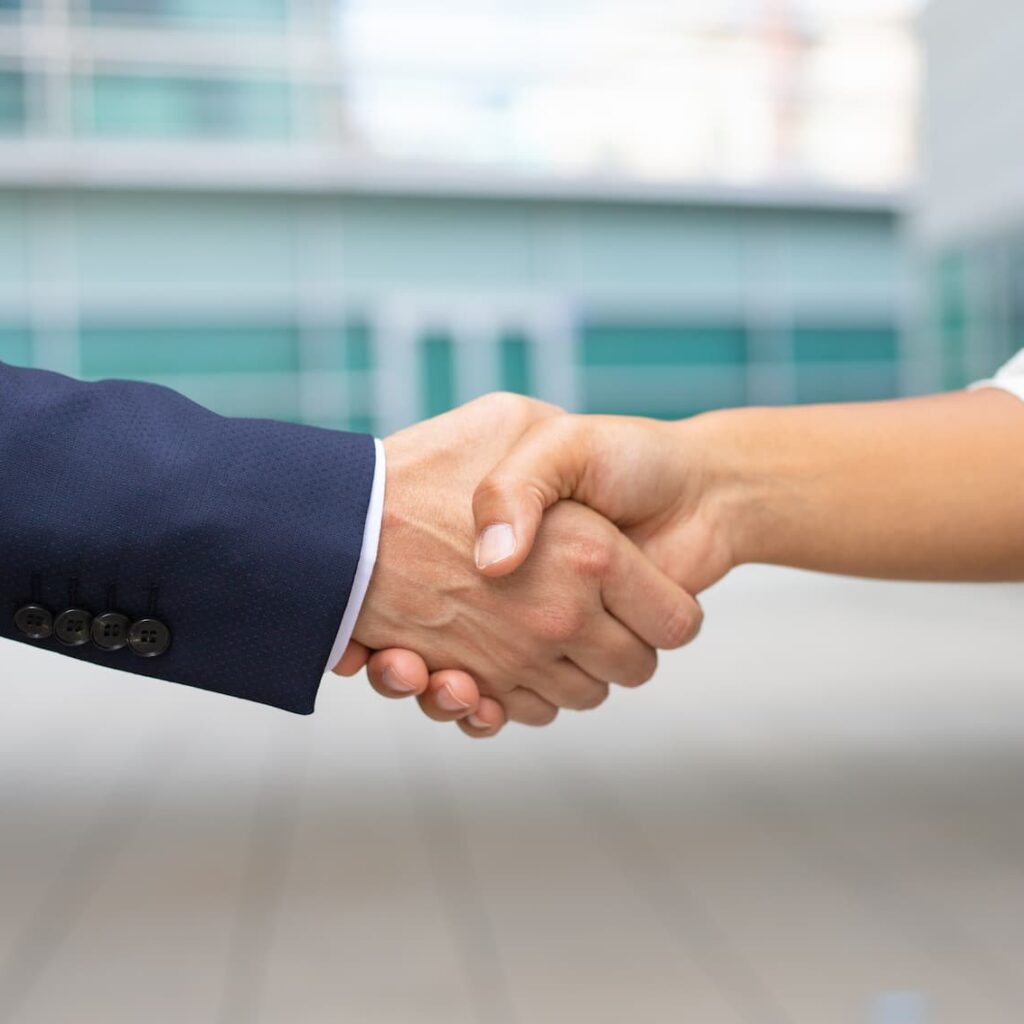 Close-up of a professional handshake between two people, symbolizing a business agreement or partnership, with a modern office building in the background.