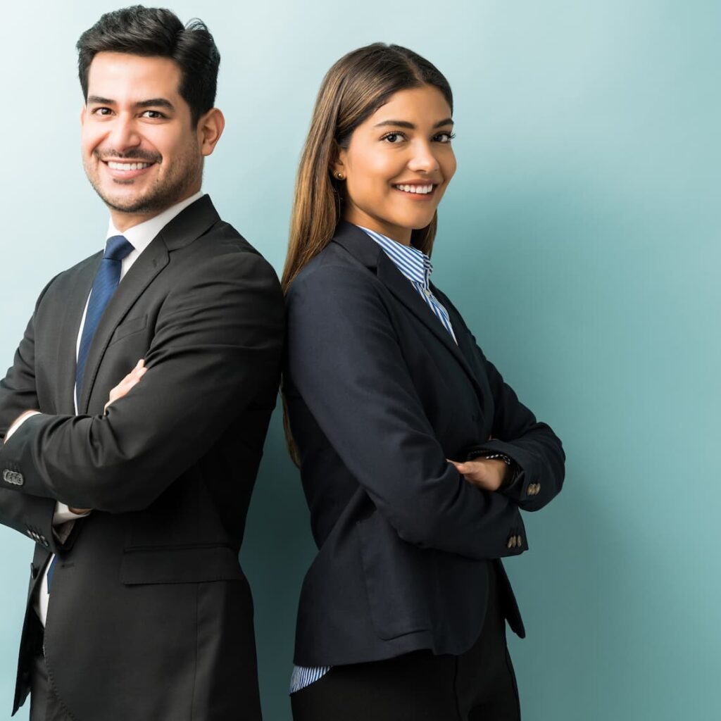 Confident business professionals, a man and a woman, standing back-to-back with arms crossed and smiling against a light blue background.